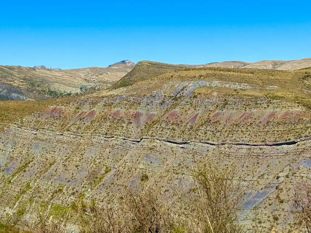 Coloured bands of rock running across a hillside above dry scrub