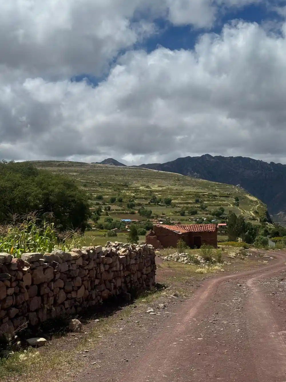 A dirt road running past a stone wall and a tiled roof in a village