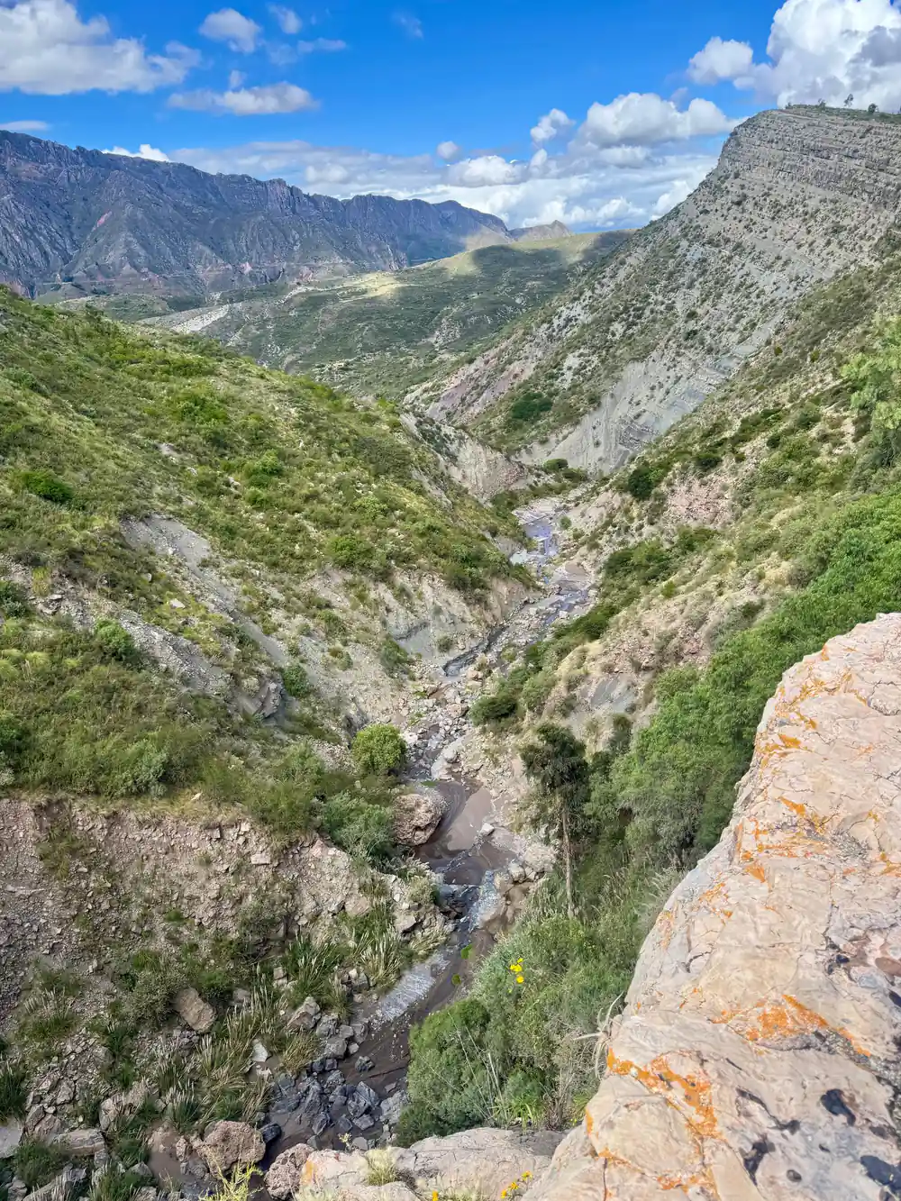 A steep gorge with orange rock and a stream at the bottom