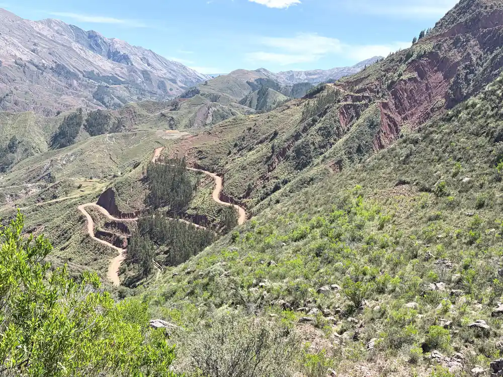 Switchbacks of an old road descending a steep green hillside