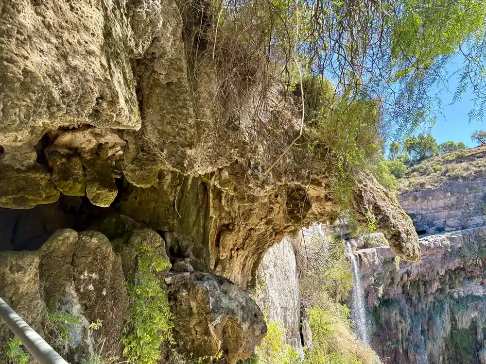 A waterfall dropping through a rock overhang hung with vegetation